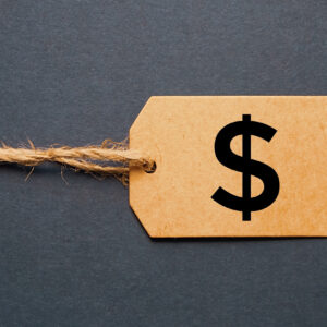 A brown cardboard price tag with a twine string and a black dollar sign symbol, influenced by the Link Tax Law, set against a dark gray background.