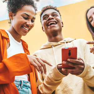 A diverse group of Gen Z friends laughing and looking at a smartphone held by a young man, outdoors under a bright, colorful background.
