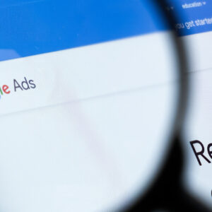 Close-up view of a computer screen displaying "Google Ads" with a magnifying glass focusing on the text "reach new customers.