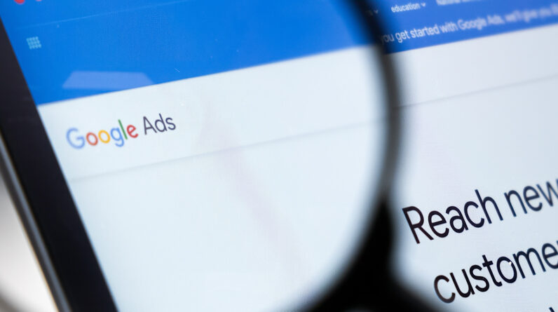 Close-up view of a computer screen displaying "Google Ads" with a magnifying glass focusing on the text "reach new customers.