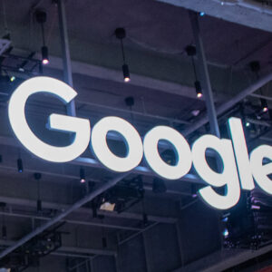 The Google logo displayed as a large, illuminated sign hanging from the ceiling in a building with an industrial-style interior.
