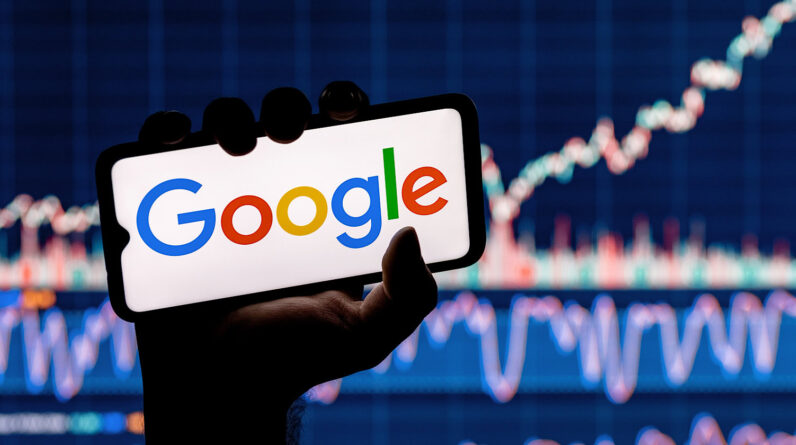 A person holding a smartphone displaying the Google Gemini Era logo, with a blurred background of stock market charts.
