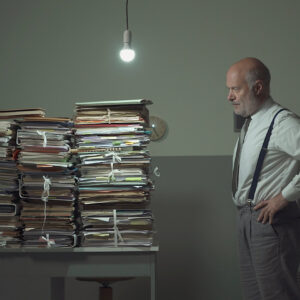 Disappointed stressed businessman staring at the stacked paperwork on his desk