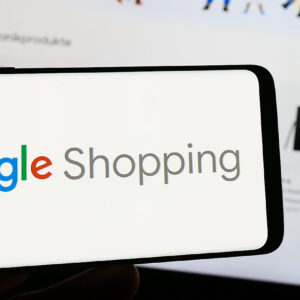 Person holding smartphone with logo of product search platform Google Shopping on screen in front of website.